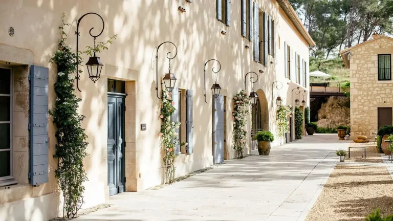Façade d'une bâtisse provençale aux volets bleus avec lanternes en fer forgé et rosiers grimpants sous une lumière douce.