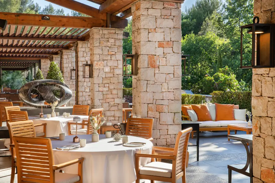 Terrasse extérieure du restaurant Le Faventia à Terre Blanche avec tables nappées de blanc, chaises en bois et piliers massifs en pierre calcaire.