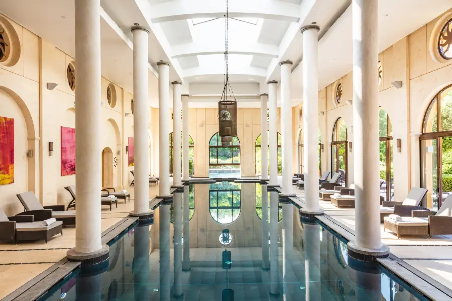Piscine intérieure du spa de Terre Blanche bordée de colonnes blanches monumentales et de lits de repos sous une verrière zénithale.